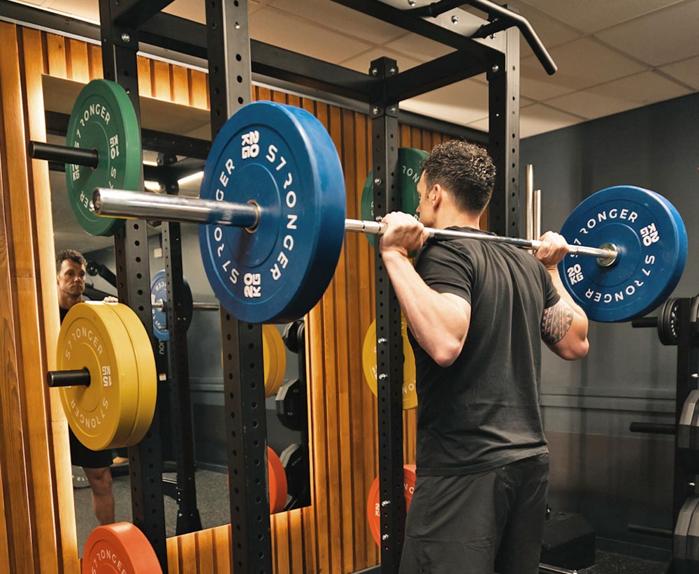 Guy training doing squats on a half rack in a home gym