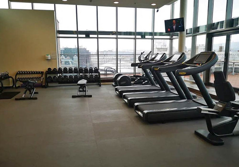 Cardio fitness room with free weights, treadmills on rubber gym floor mats, overlooking a large window view in the background