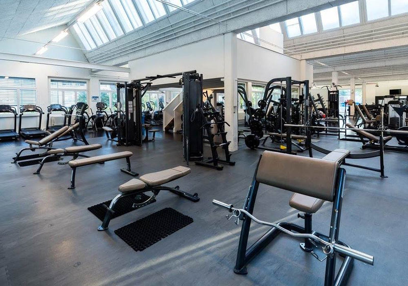 Large gym interior with fitness machines, benches, cardio machines and a rubber gym floor