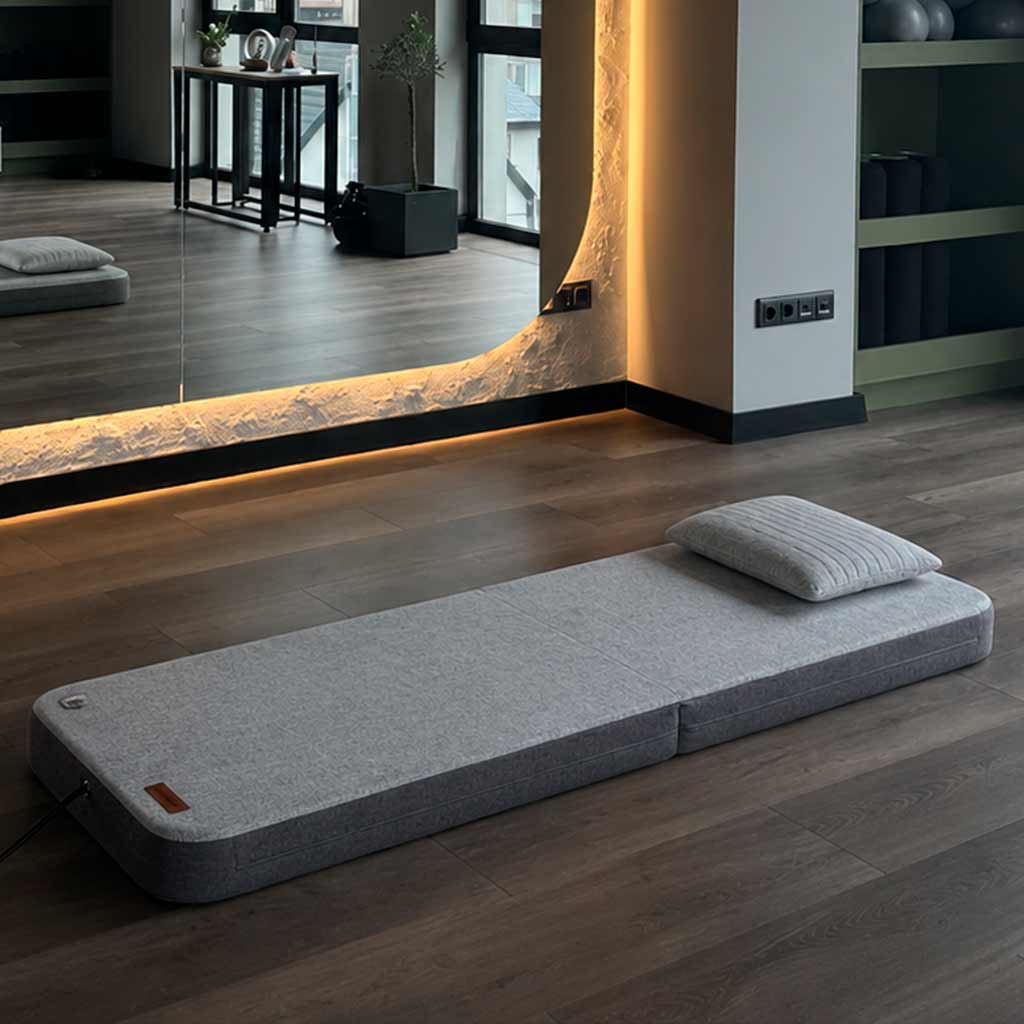 Neurosonic floor mat with pillow on a wooden floor in a modern room.